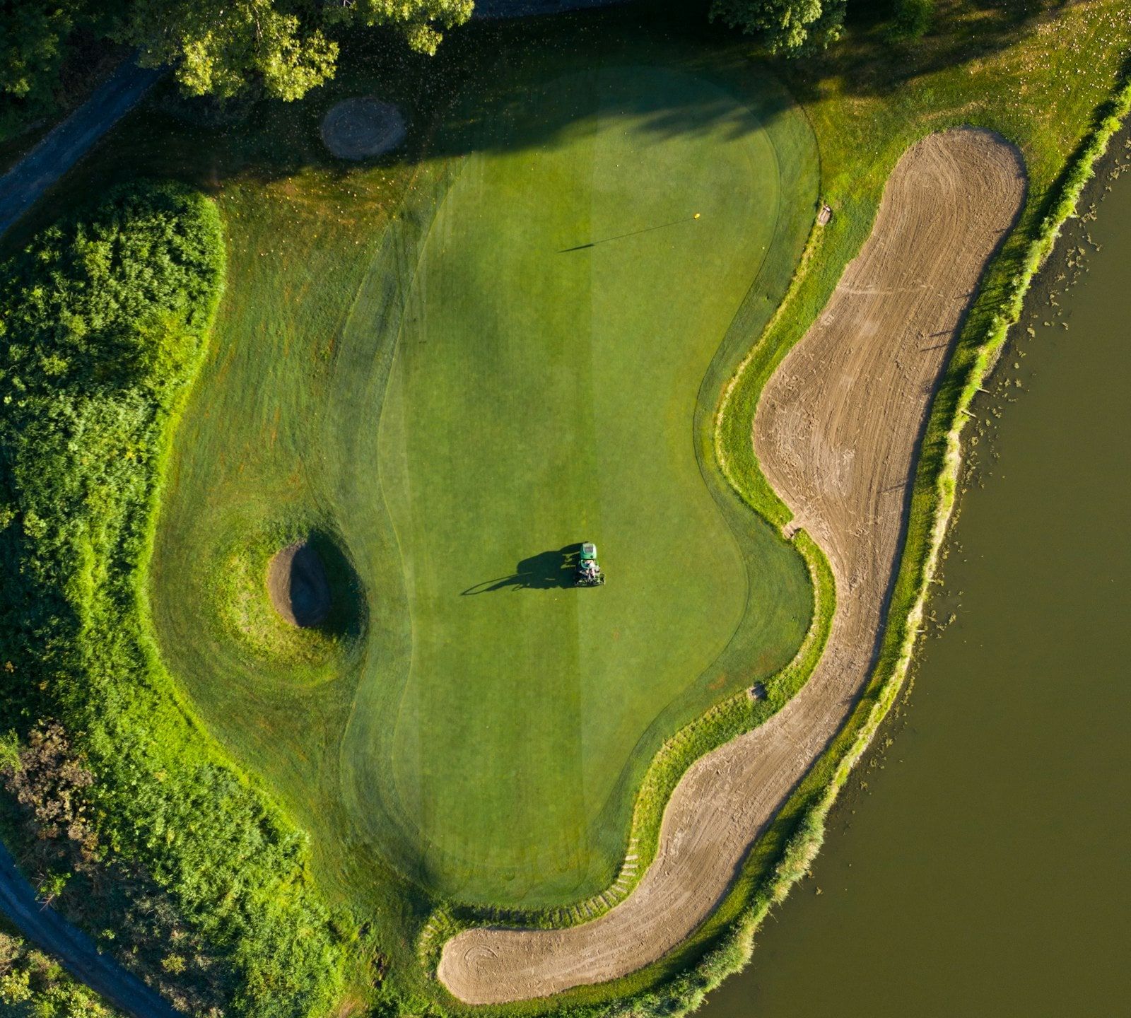 A golf green from above, with a mower and a long curving sand bunker